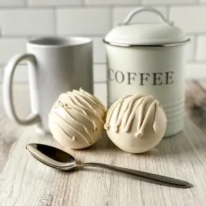 white chocolate coffee bombs with spoon, mug, and coffee canister
