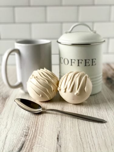 white chocolate coffee bombs with spoon, mug, and coffee canister