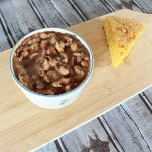 vertical image of instant pot black eyed peas in a bowl with wedge of cornbread