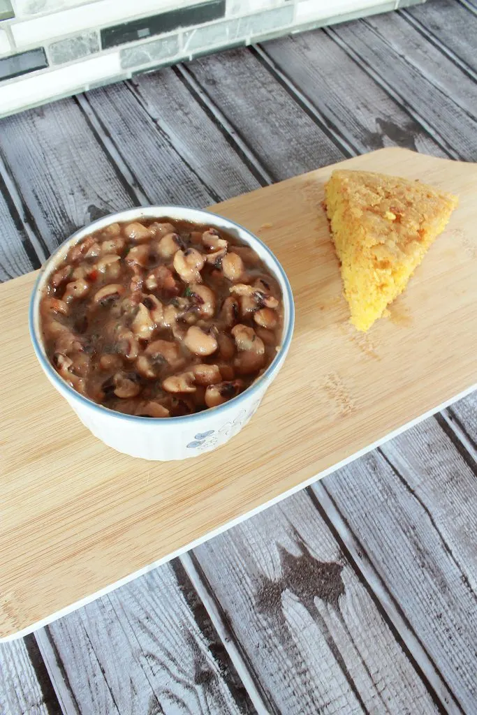 vertical image of instant pot black eyed peas in a bowl with wedge of cornbread