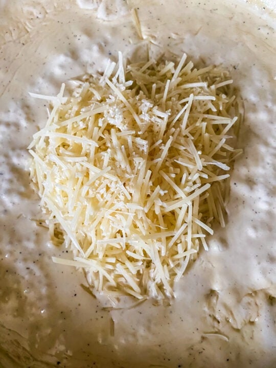 Adding parmesan cheese into thickened creamy rasta sauce