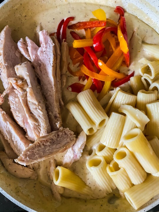 adding noodles, peppers, and chicken into the creamy rasta sauce