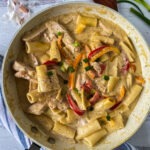 Creamy gluten free rasta pasta in a skillet with wooden spoon and scallions