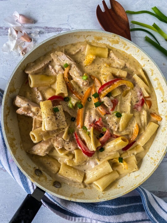 Creamy gluten free rasta pasta in a skillet with wooden spoon and scallions
