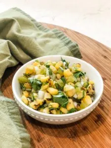 bowl of fire-roasted corn salsa on wooden cutting board with green tea towel