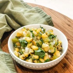 bowl of fire-roasted corn salsa on wooden cutting board with green tea towel
