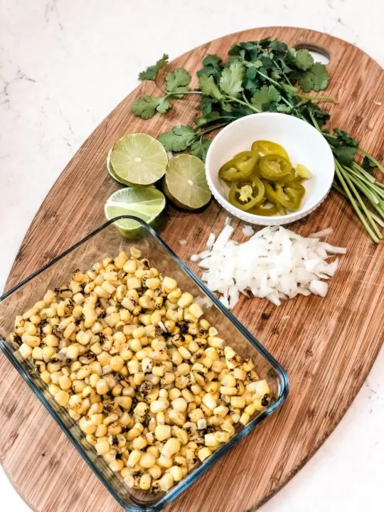 ingredients for gluten free corn salsa bowl of fire roasted corn chopped onion, sliced jalapenos, sliced limes, and fresh cilantro