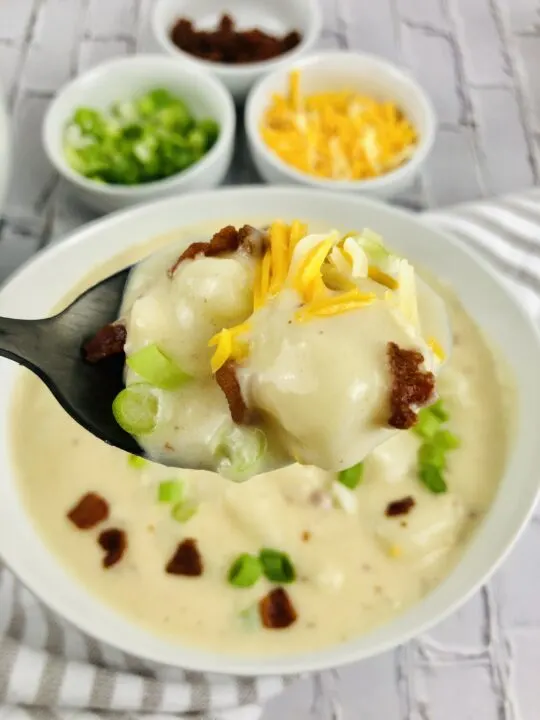 close up of spoon full of loaded baked potato soup topped with potato, green onion, cheddar cheese, and bacon