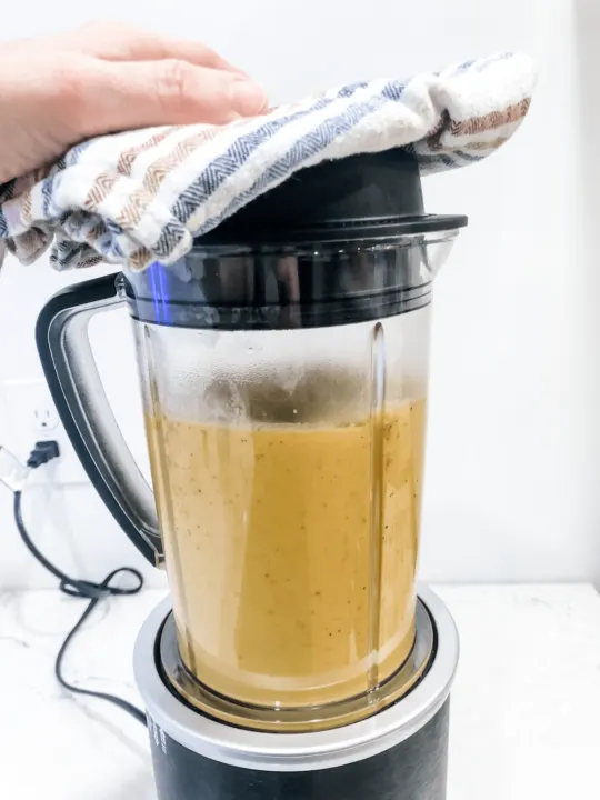blending dairy free gluten free cheese sauce in blender with dish towel over top
