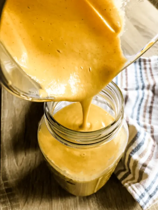 pouring gluten free dairy free cheese sauce from blender pitcher into large mason jar