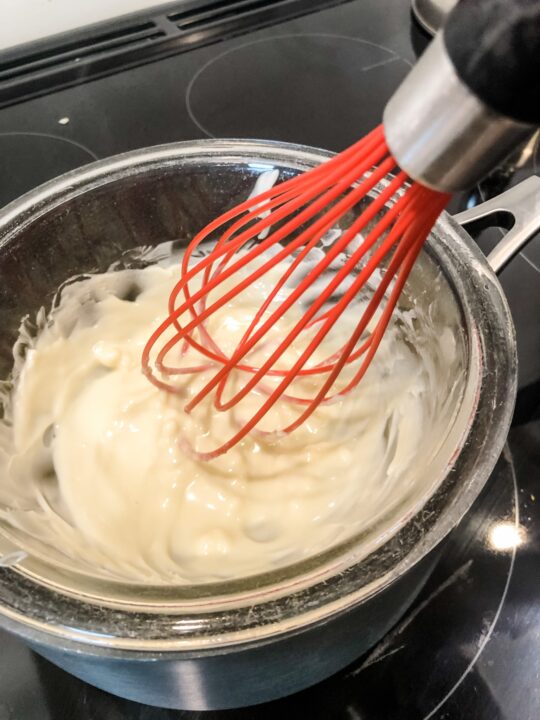 Melting vegan white chocolate in double broiler with red whisk