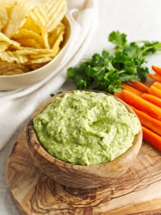 White Bean Green Goddess Dip in wooden bowl with carrots parsley and chips