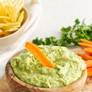 White Bean Green Goddess Dip in wooden bowl with carrots and chips