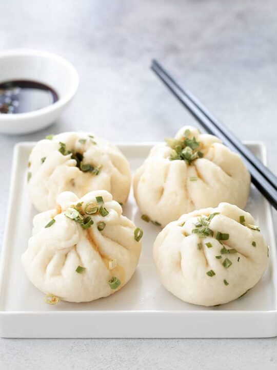 chinese meat buns on a square plate with soy sauce and chives with bowl of gf soy sauce