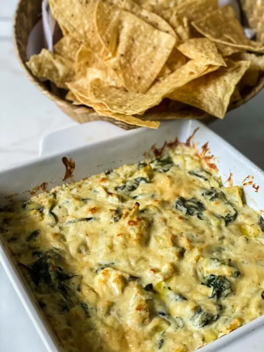 baked spinach artichoke dip out of oven with tortilla chips on marble counter