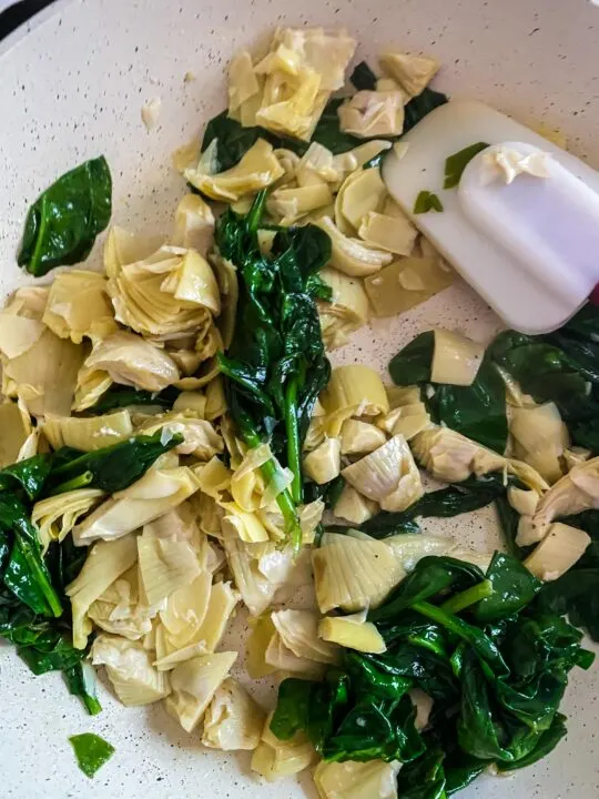 cooking spinach and artichokes in the pan with spatula