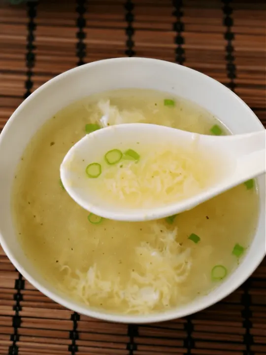 egg drop soup in bowl with spoon on bamboo mat