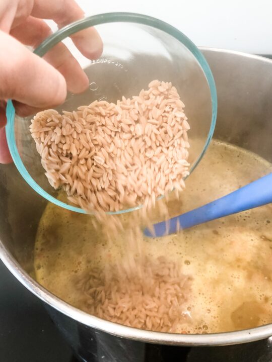pouring gluten free orzo into pot of soup on stove