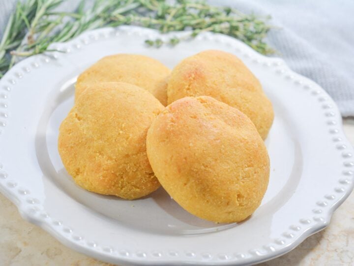 4 gluten free pumpkin bread rolls on a white plate with thyme and gray napkin