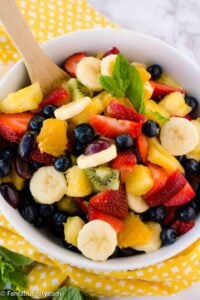 gluten free dairy free honey lime fruit salad in bowl with wooden spoon and yellow towel