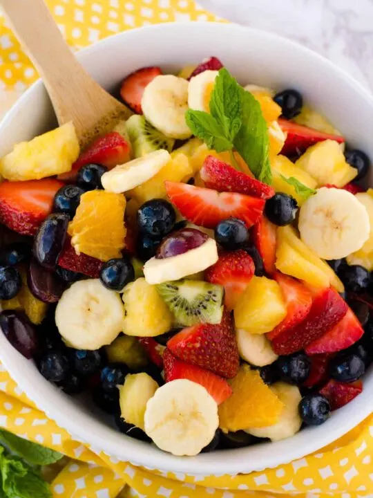 gluten free dairy free honey lime fruit salad in bowl with wooden spoon and yellow towel