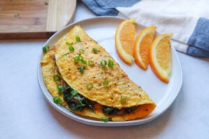 spinach and mushroom omelet on plate with orange slices