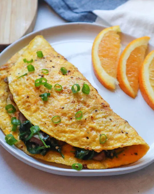 spinach and mushroom omelet on plate with orange slices