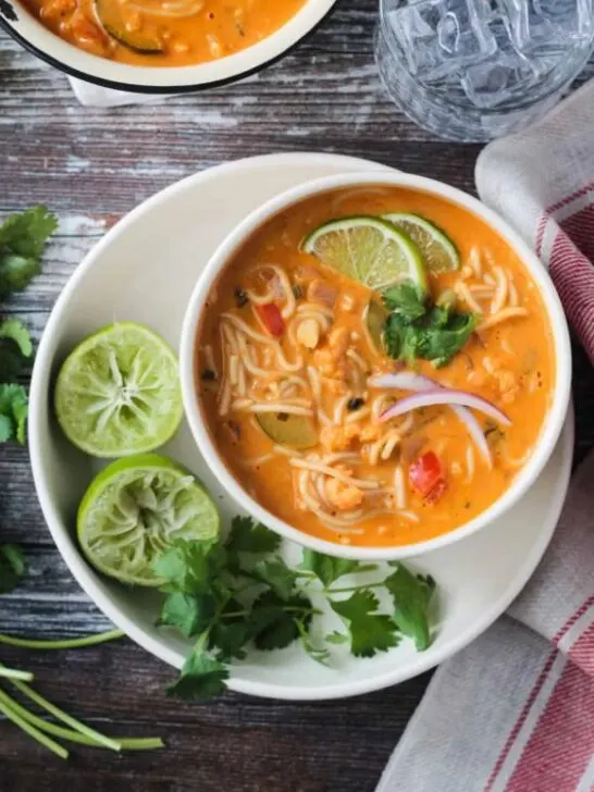 gluten free red curry thai noodle soup in white bowl with limes and cilantro