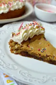 gluten free chocolate chip cookie cake with sprinkles and frosting on white plate
