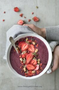healthy acai smoothie bowl topped with strawberries held up by hands