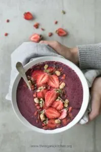 healthy acai smoothie bowl topped with strawberries held up by hands