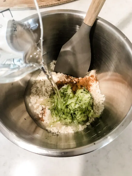 mixing ingredients for healthy zucchini pancakes in metal mixing bowl