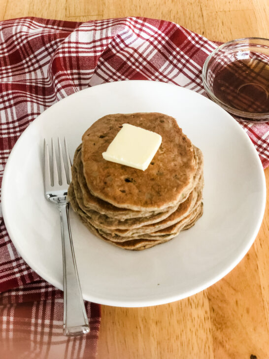 stack of healthy protein pancakes with pat of butter on white plate with red checkered tea towel and maple syrup in dish
