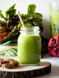 superfood green detox smoothie in mason jar with pomegranate and beets in background