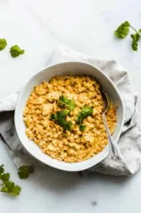 vegan coconut red lentil dahl in white bowl with spoon topped with parsley