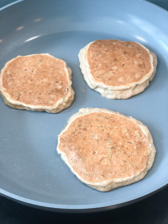 3 high protein zucchini pancakes cooking in nonstick green pan