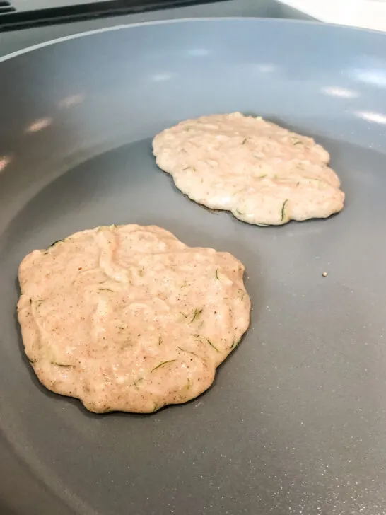 two gluten free zucchini pancakes cooking in nonstick green pan