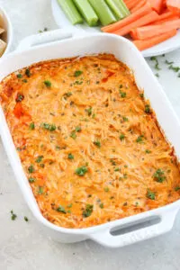 gluten free buffalo chicken dip in casserole dish with celery and carrot sticks