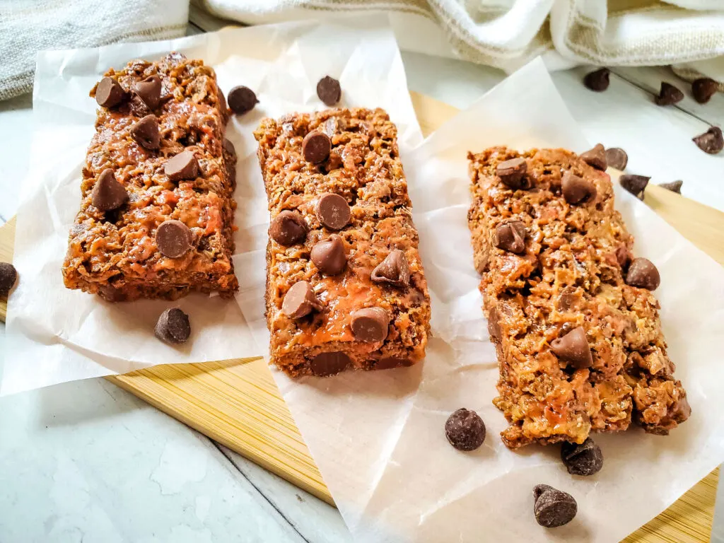 3 Chocolate Nut-Free Protein Bars with chocolate chips on parchment and wooden board.