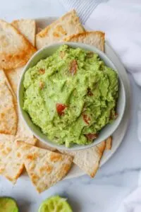 bowl of homemade guacamole with homemade chips in background on plate