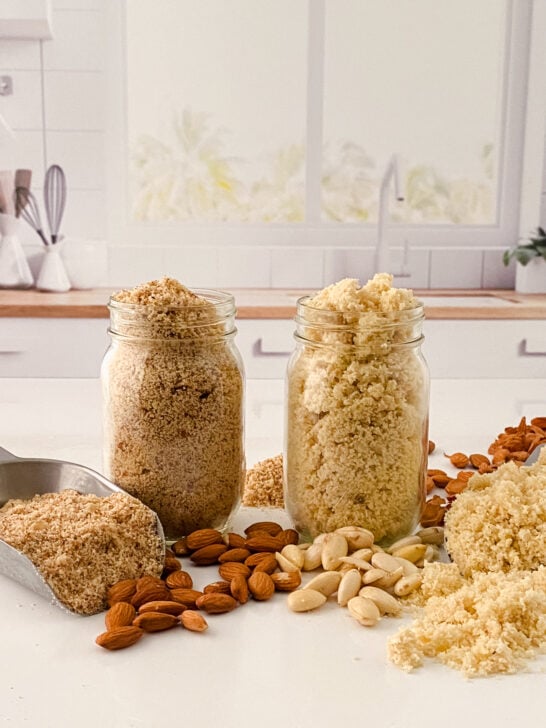 jar of blanched almond flour and jar of almond meal on kitchen counter with almonds scattered