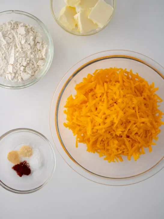 ingredients for homemade goldfish crackers in glass bowls: shredded cheddar cheese, gluten free flour, butter, and seasonings.