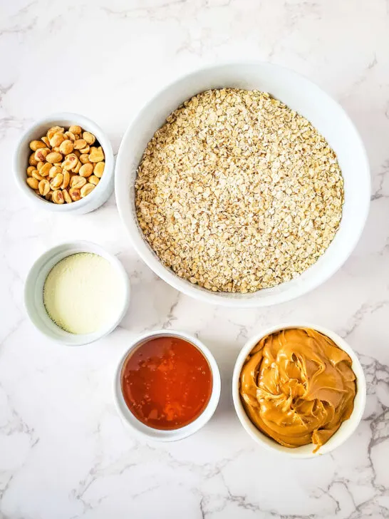 Ingredients to make no bake protein bars, bowl of gluten free oats, peanuts, protein powder, honey, peanut butter