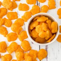 landscape image of gluten free goldfish crackers in white bowl with more crackers scattered on weathered white wood