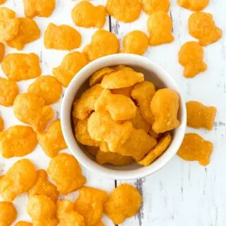 gluten free goldfish crackers in white bowl with more crackers scattered on weathered white wood