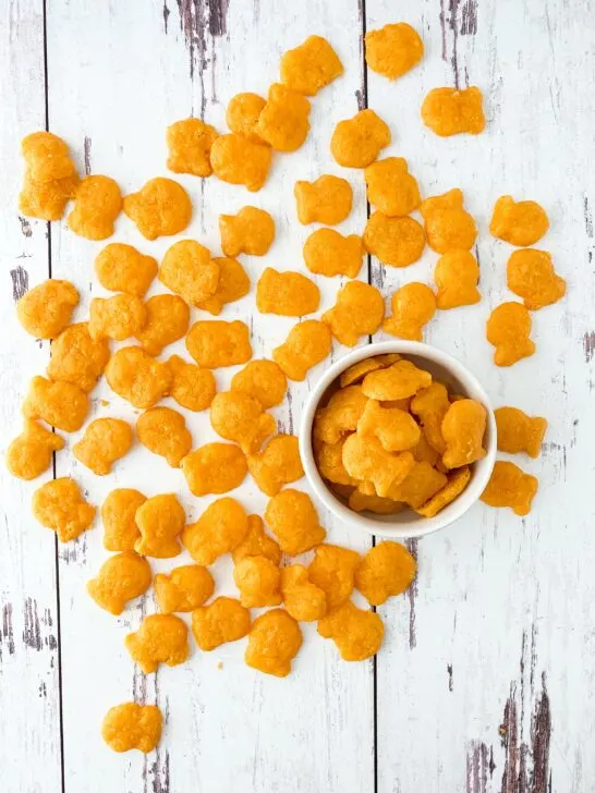 homemade gluten free goldfish crackers scattered on weathered wood with goldfish in little white bowl
