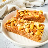 Finished dairy free gluten free no bake peanut protein bars on white plate with tea towel and peanuts in background