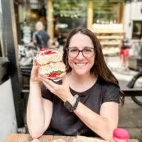 Sharon McCaskill from The Helpful GF holding up a gluten free bagel with vegan cream cheese and veggies in front of modern bread and bagel in NYC