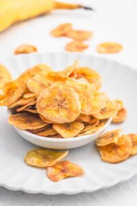 air fryer banana chips on white bowl overflowing onto white plate