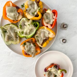 image of prepared philly cheesesteak stuffed peppers on white plate with a small white plate with one pepper and salt and pepper shakers